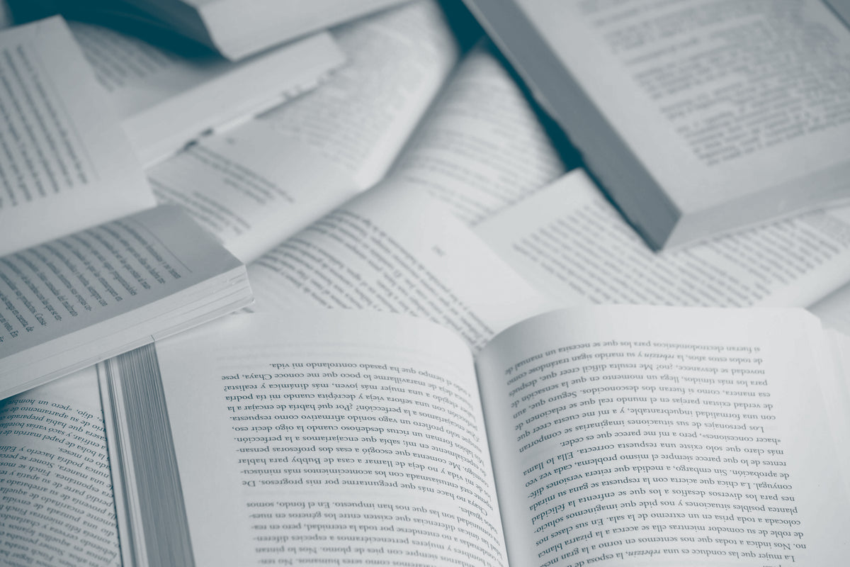 Multiple books sit open on top of each other, at different angles showing paragraphs of text, likely from novels.