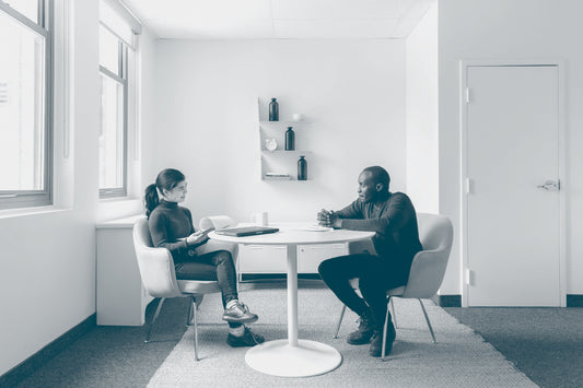 A man and woman are in conversation during a meeting at a round table on comfortable chairs in a modern room. 